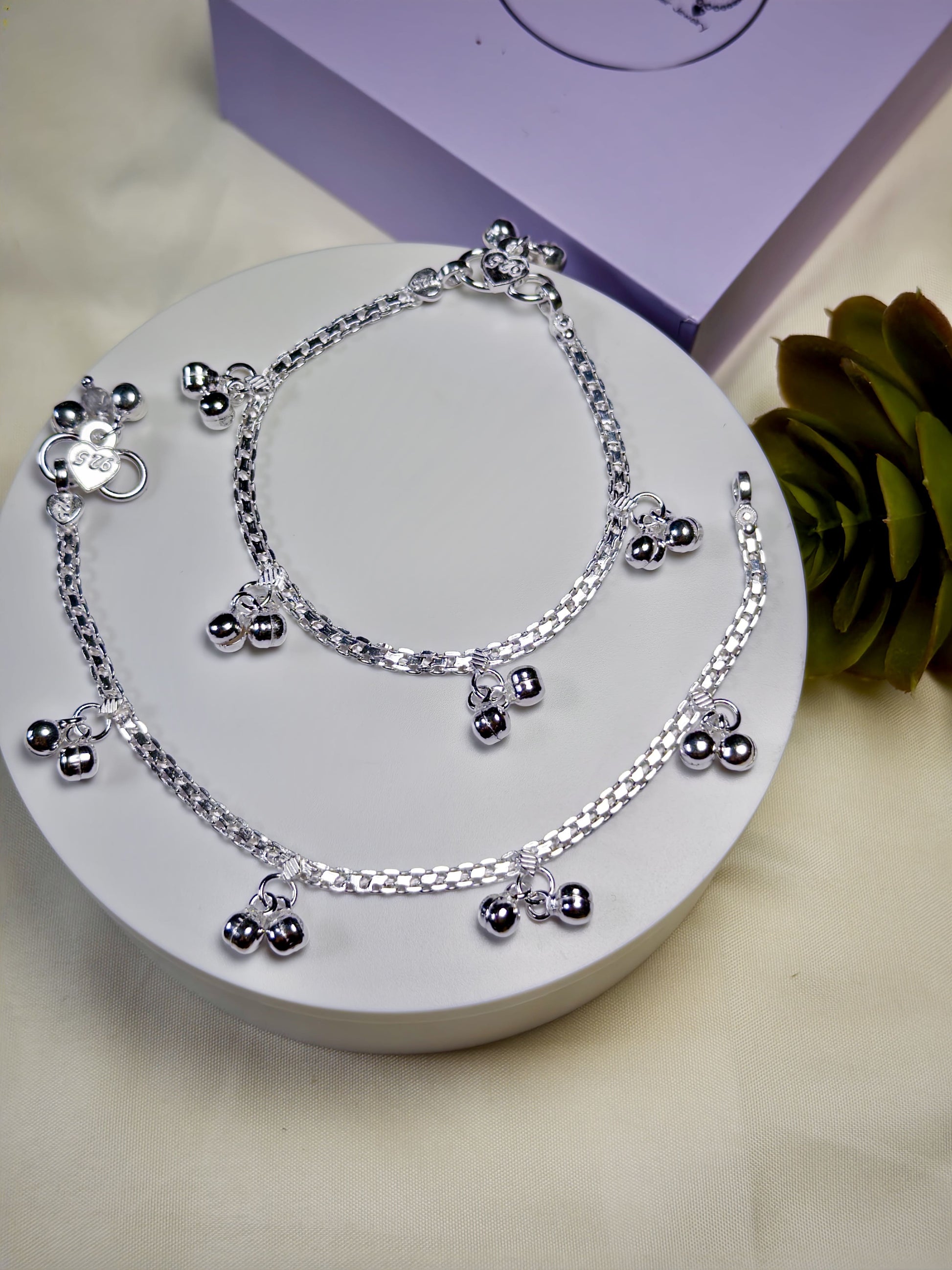 Kids silver anklets with charms on a white surface
