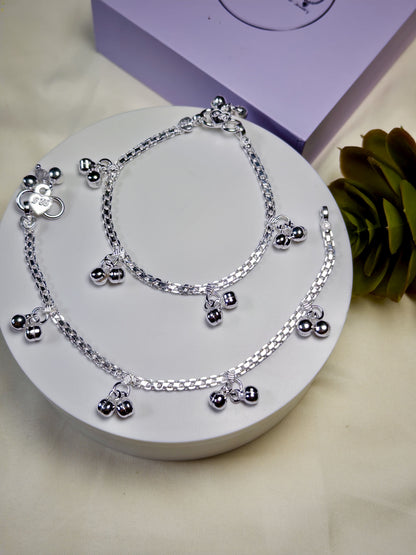Kids silver anklets with charms on a white surface