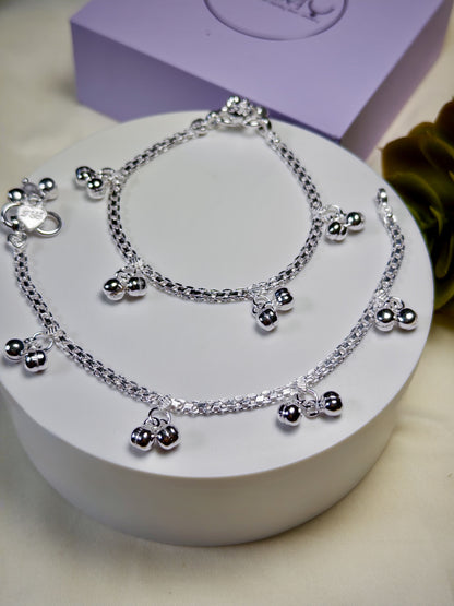 Kids silver anklets with heart-shaped charms on a white stand with a purple box in the background.