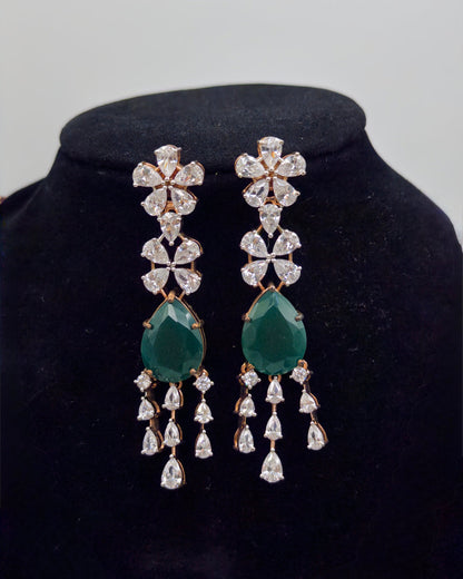 Pair of earrings with green teardrop and diamond-like stones on a black velvet stand.
