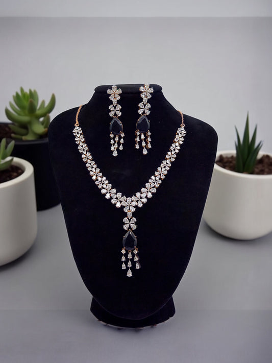 Jewelry set with necklace and earrings on a black velvet stand, with potted plants in the background.