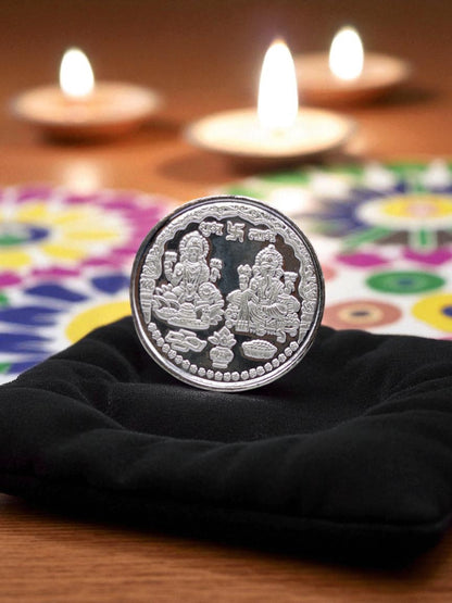 Silver coin with Lakshmi Ganesh design on a black cloth with candles in the background