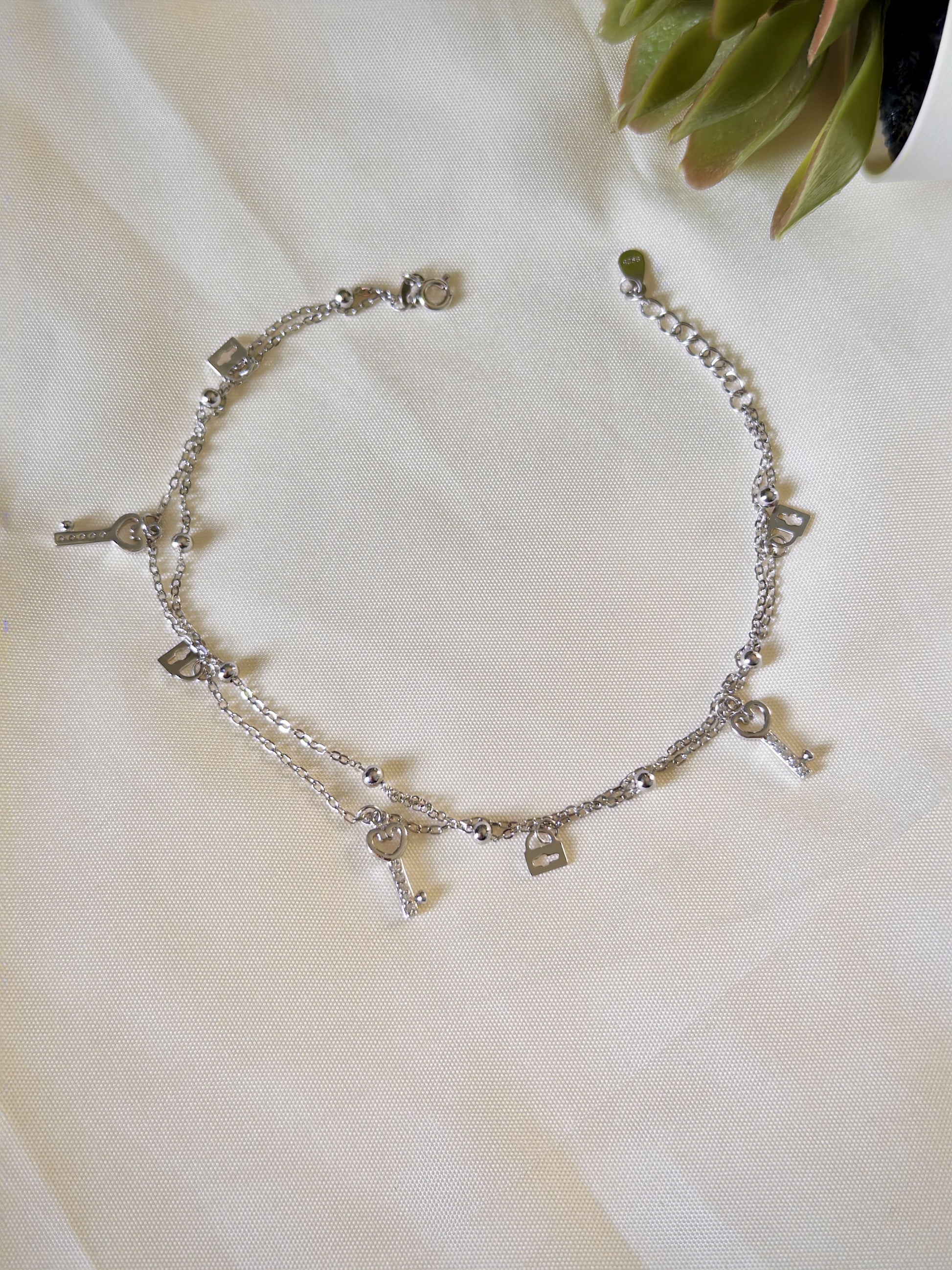 Silver anklet with lock & key charms on a white fabric background