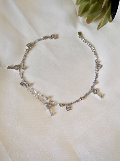 Silver anklet with lock & key charms on a white fabric background