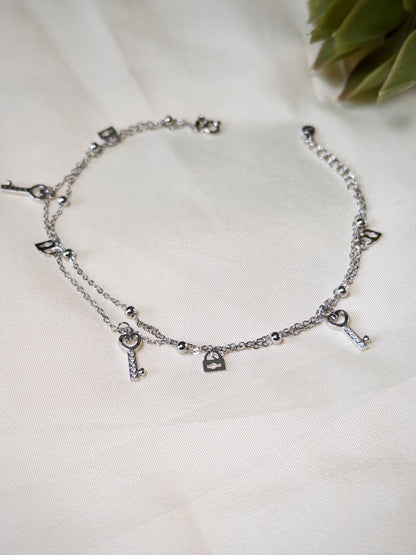 Silver anklet with various charms on a white fabric background