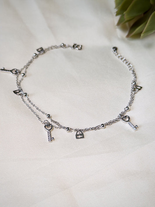 Silver anklet with various charms on a white fabric background