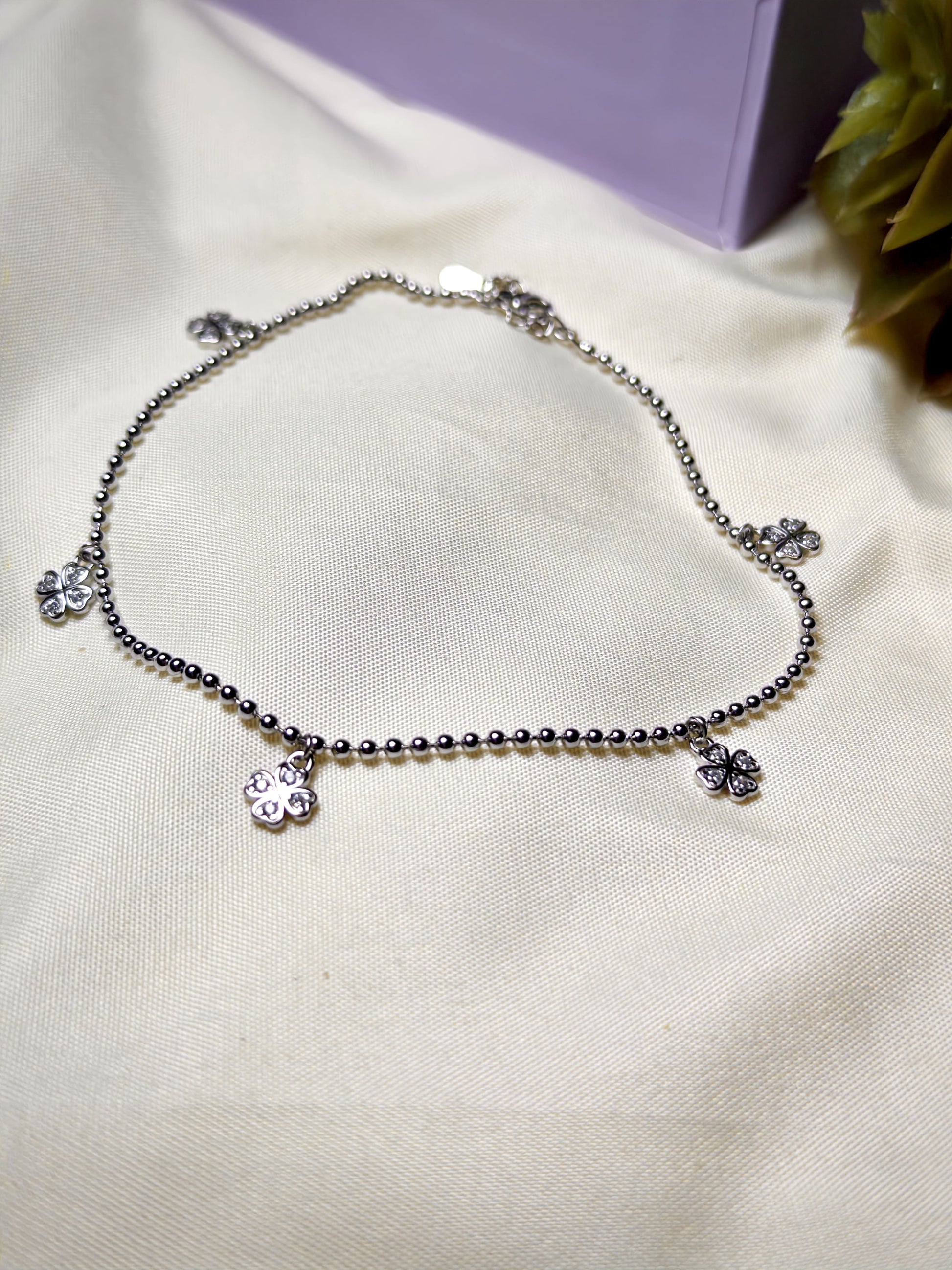 Silver anklet with flower charms on a light fabric background
