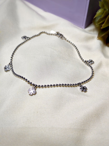 Silver anklet with flower charms on a light fabric background
