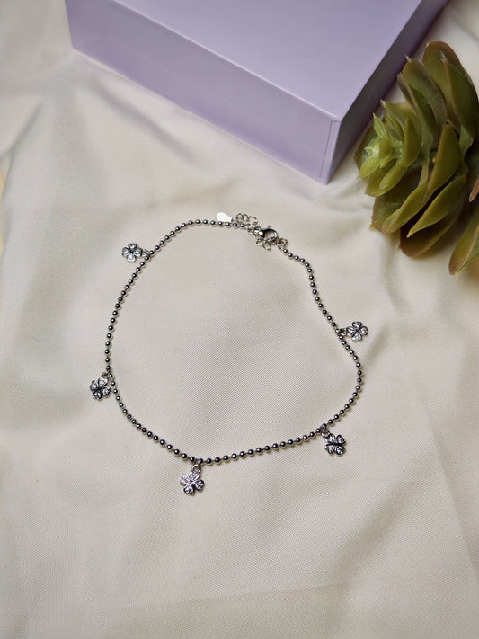 Silver anklet with floral charms on a light surface