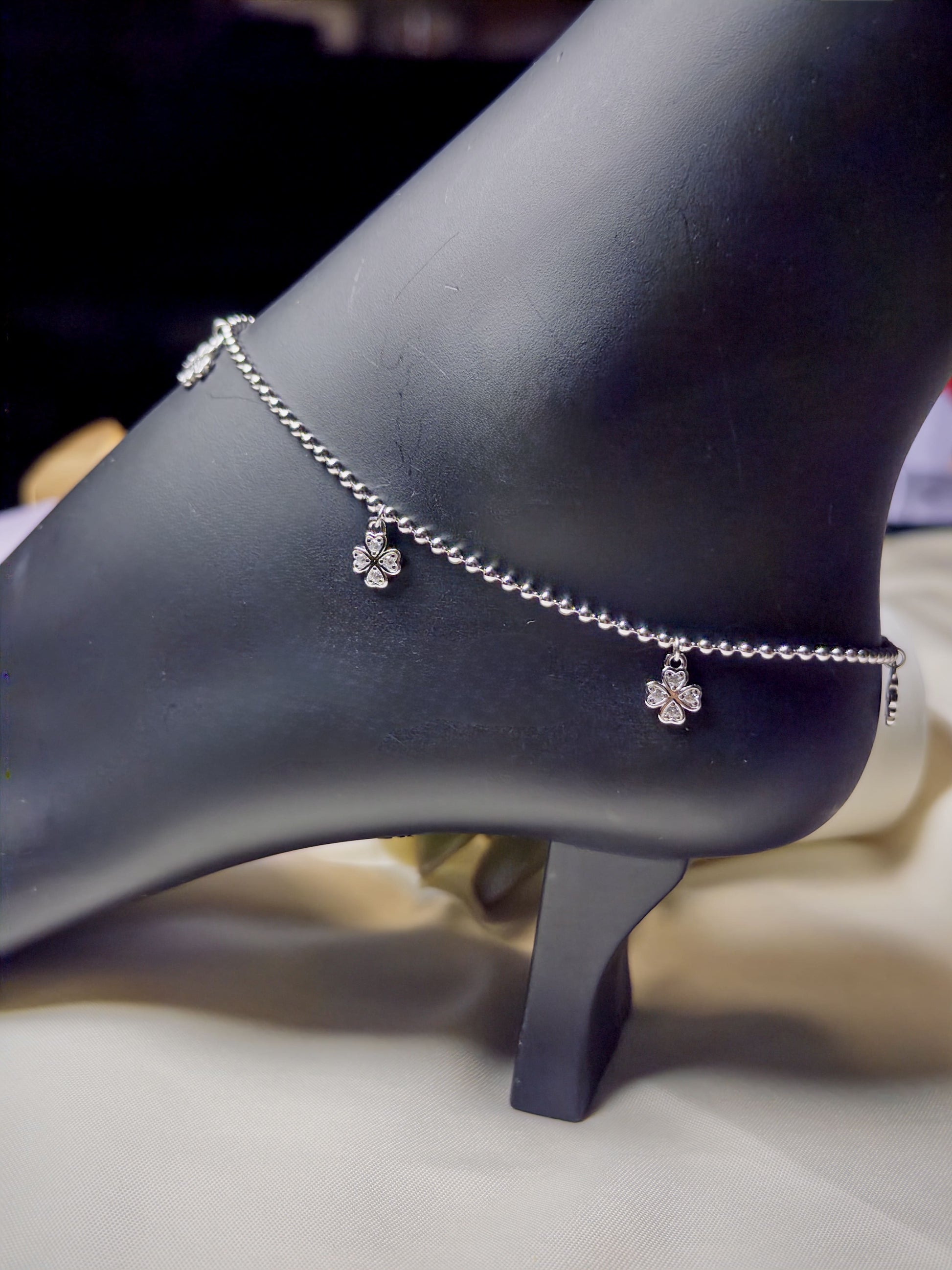 Silver anklet with floral charms on a mannequin foot.