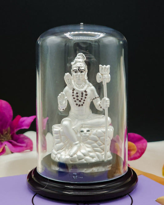 Silver statue of a Lord Shiva inside a glass dome with pink flowers in the background