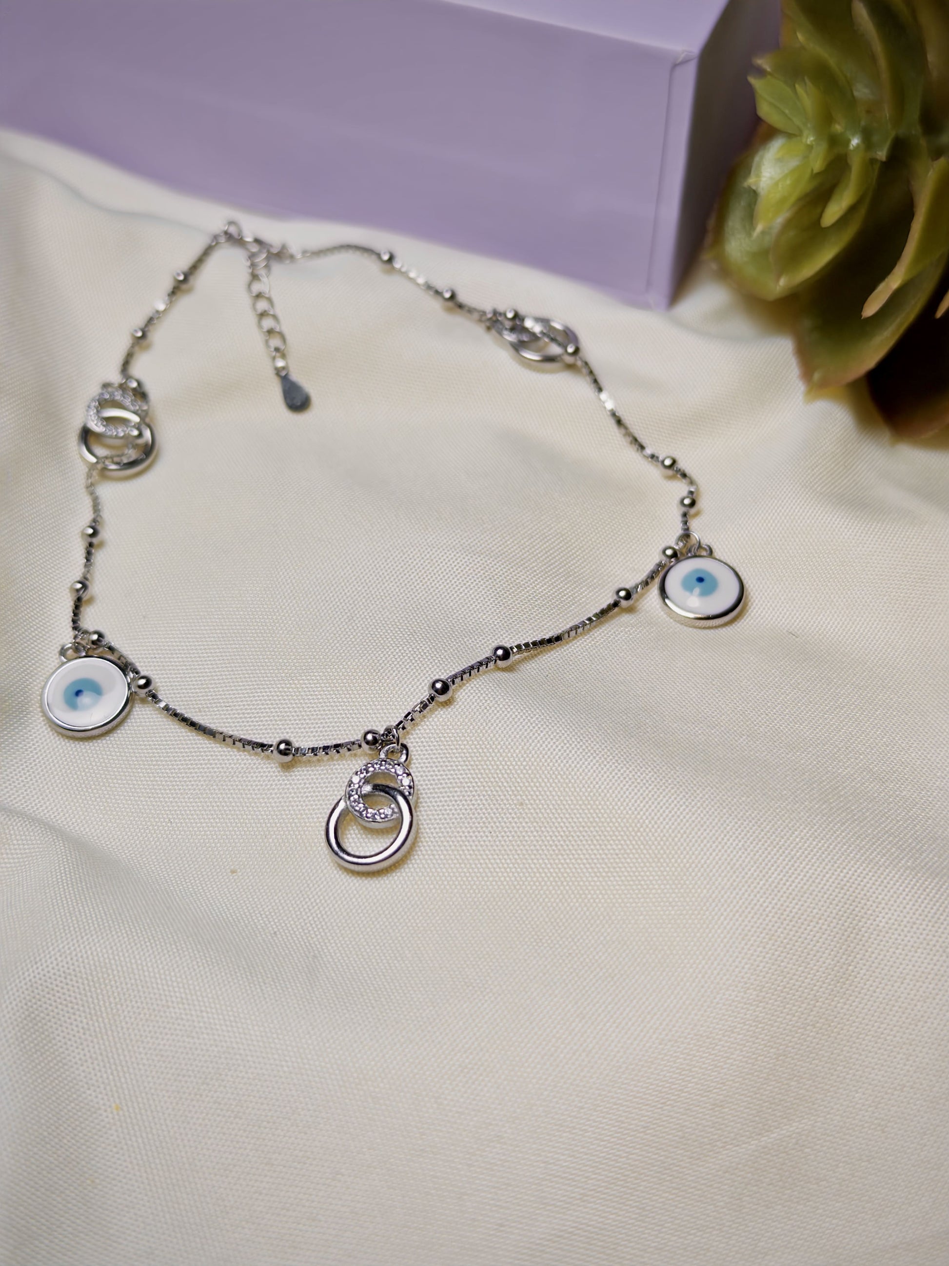 Silver anklet with eye-shaped charms on a light fabric background