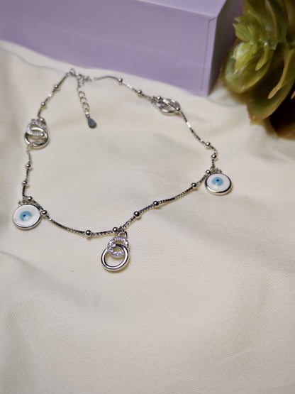 Silver anklet with eye-shaped charms on a light fabric background