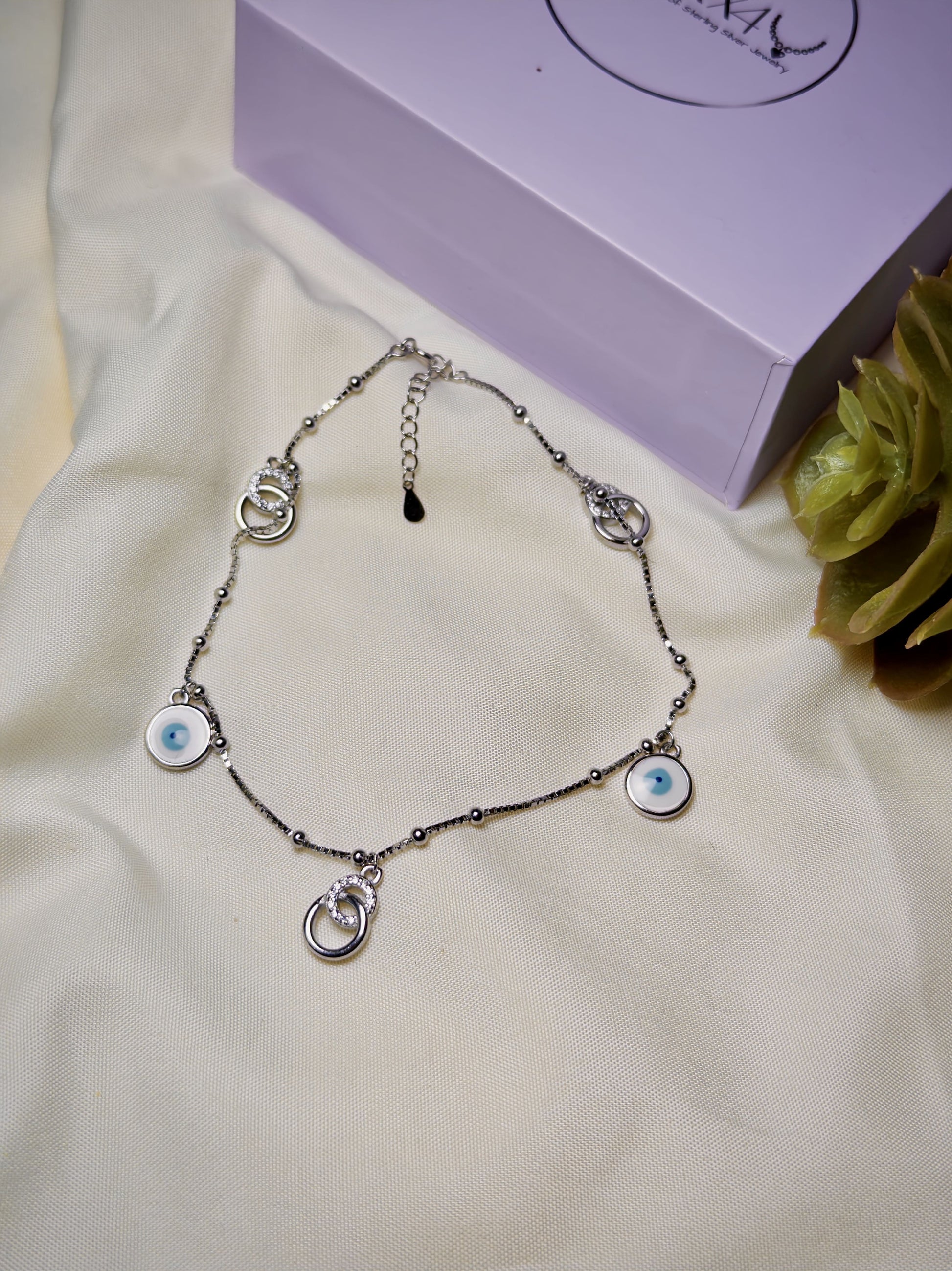 Silver anklet with eye-shaped charms on a white fabric background