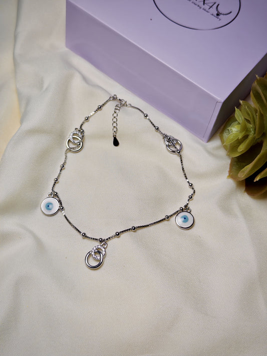 Silver anklet with eye-shaped charms on a white fabric background