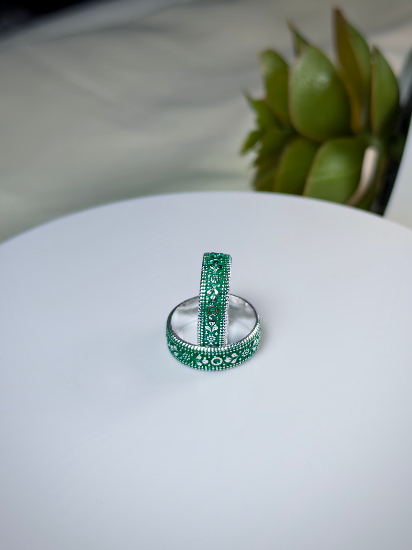 Two green toe rings on a white surface with a blurred plant in the background
