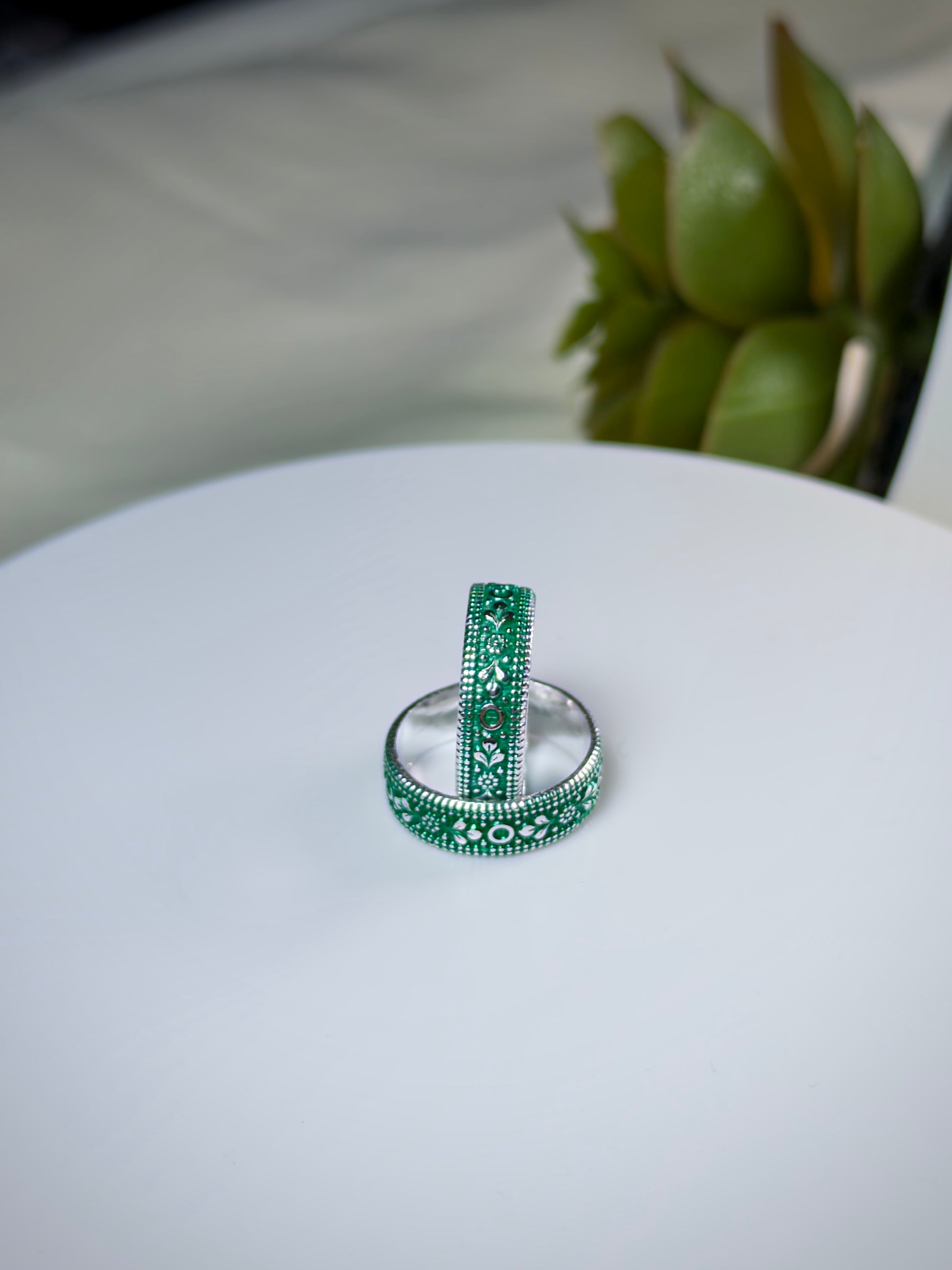 Two green toe rings on a white surface with a blurred plant in the background