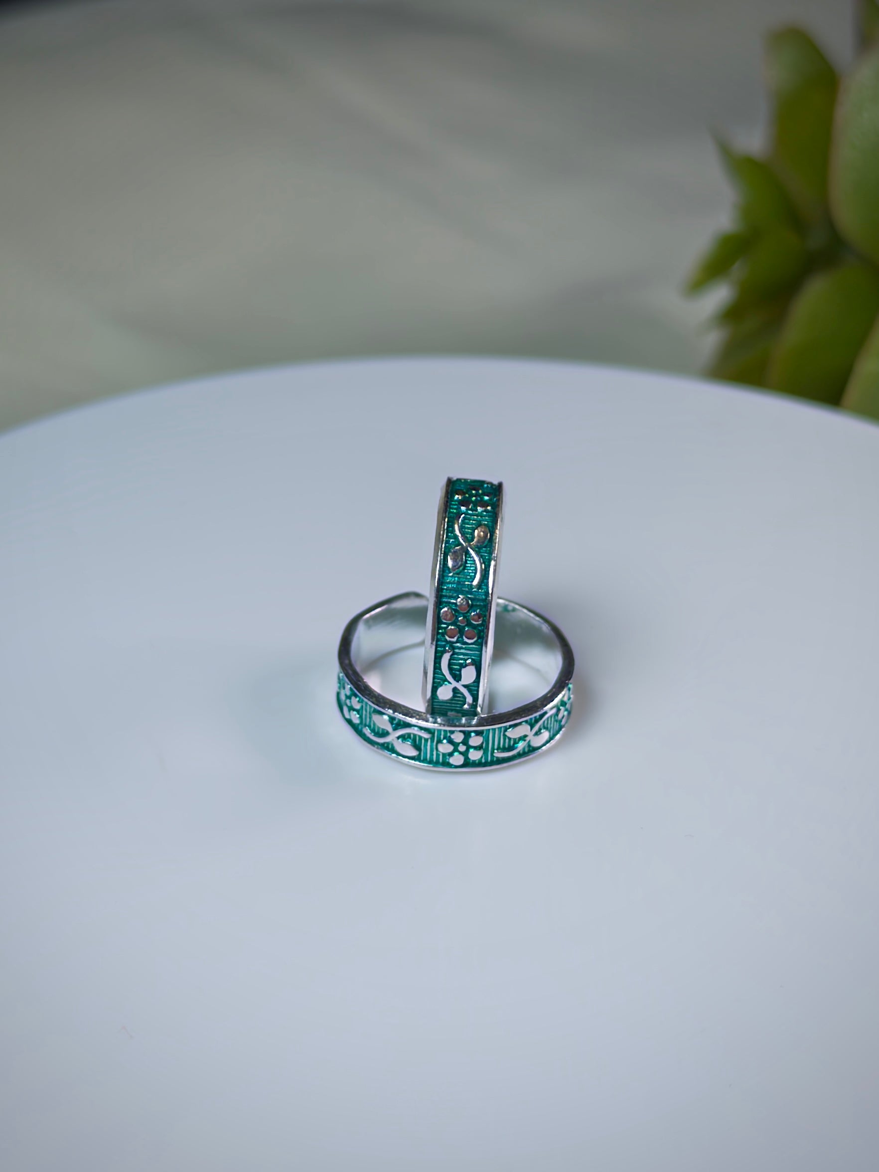 Two green toe rings on a white surface with a blurred background