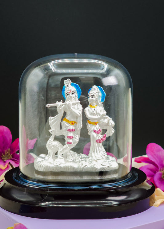 Radha Krishna Idol inside a glass dome with pink flowers in the background