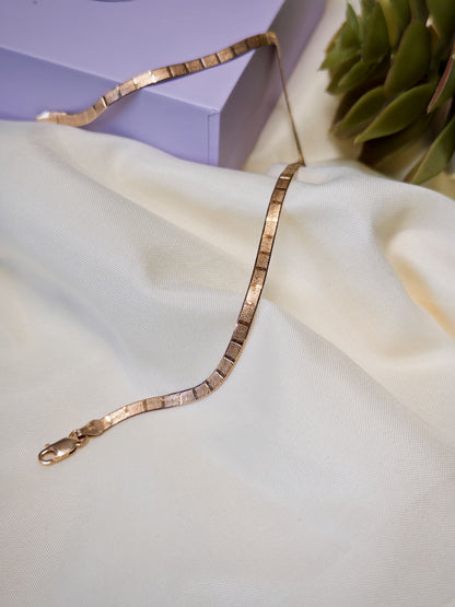Rose gold anklet on a light fabric surface with a blurred background