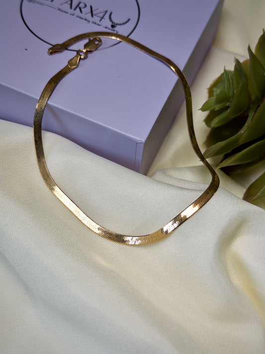 Rose gold anklet on a white fabric surface with a purple box in the background