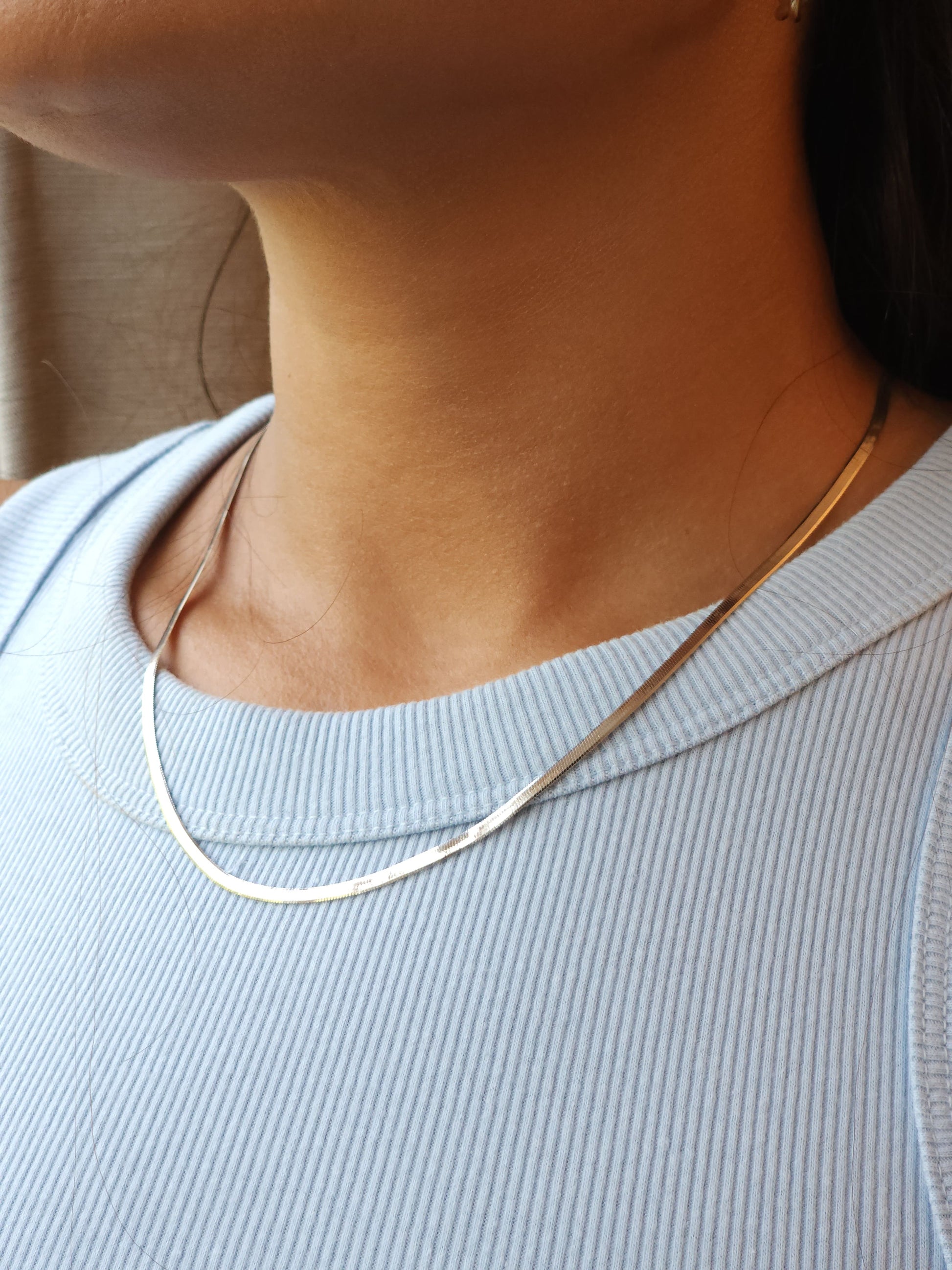 Close-up of a person wearing a light blue ribbed top with a SILVER HERRINGBONE CHAIN