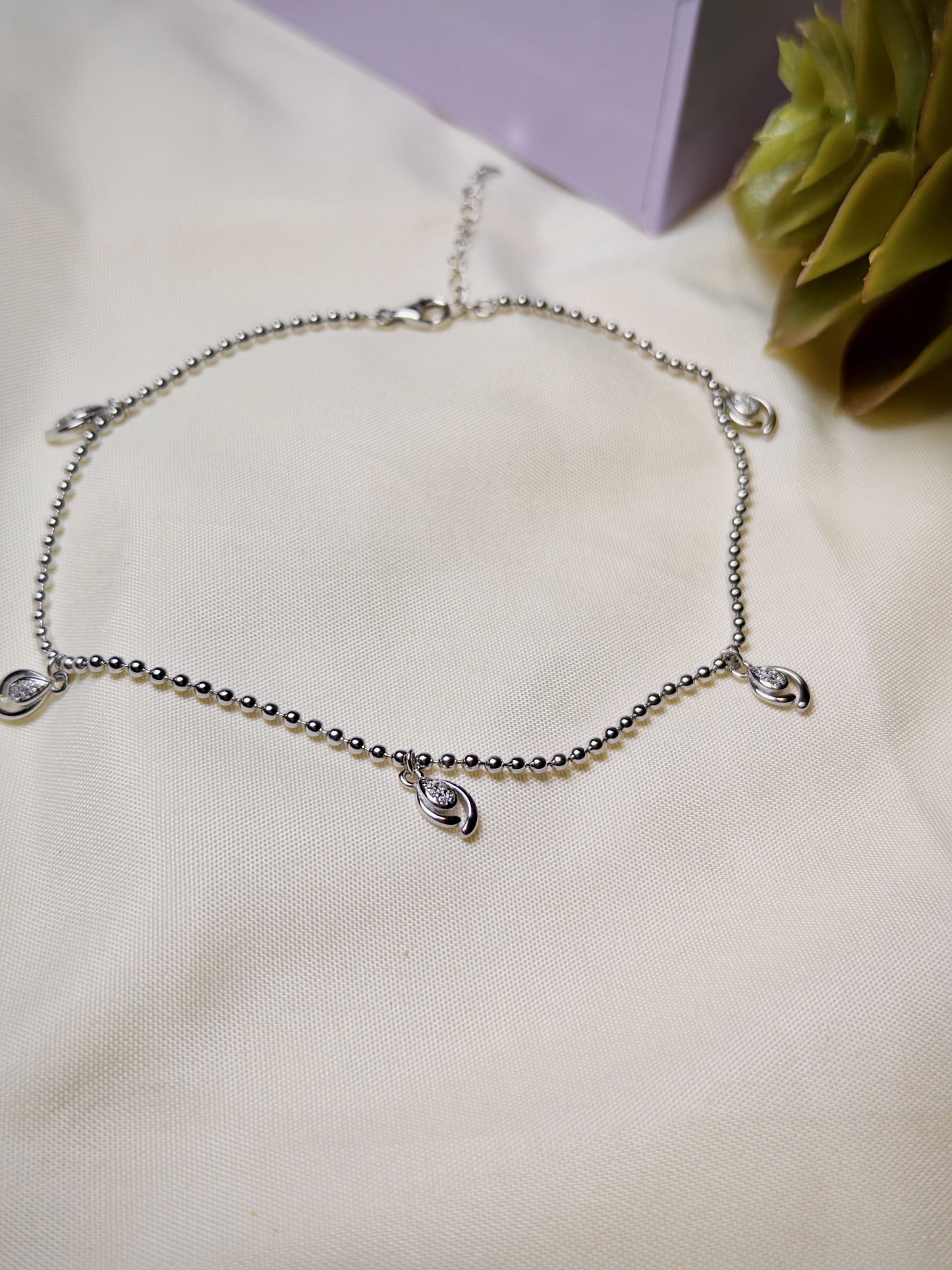 Silver anklet with raindrop-shaped charms on a light fabric background