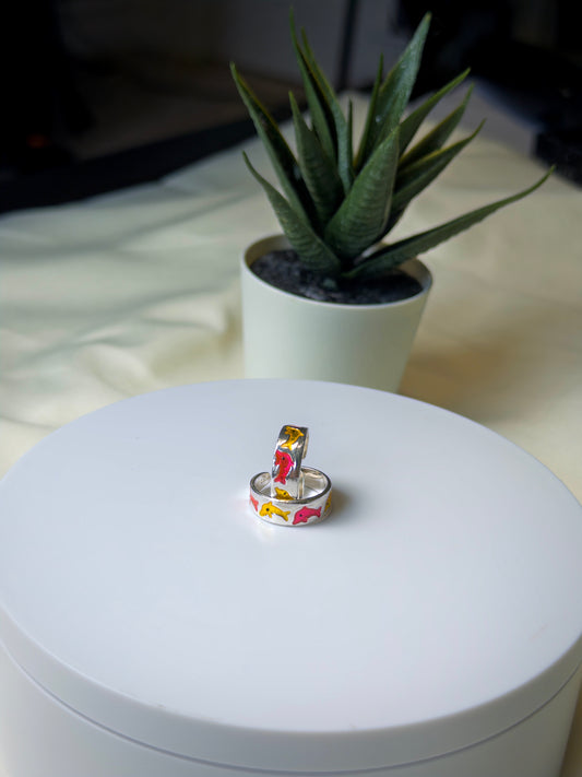 Silver Toe ring with fish design on a white surface, potted plant in the background