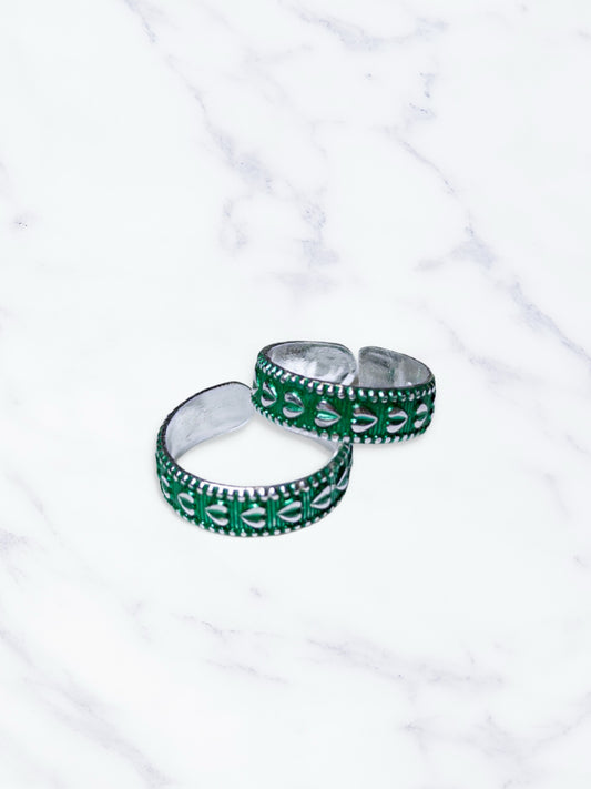Two green and silver toe rings on a white marble surface