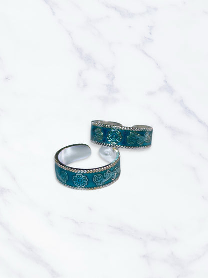 Two turquoise patterned toe rings on a white marble surface