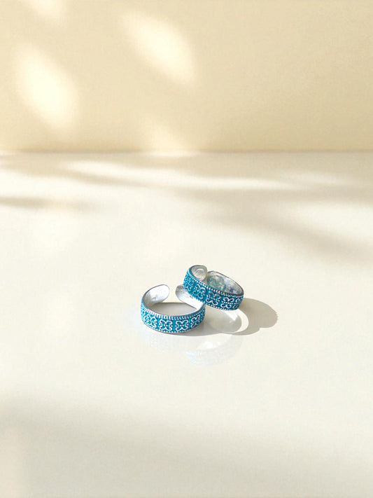 Pair of blue patterned toe rings on a light beige surface
