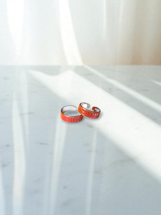 Two orange toe rings on a marble surface with a white curtain in the background