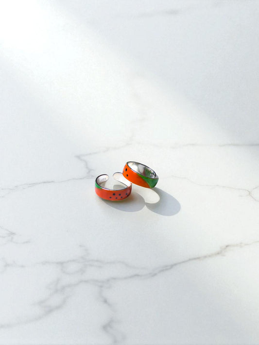 Two colorful watermelon-themed toe rings on a marble surface