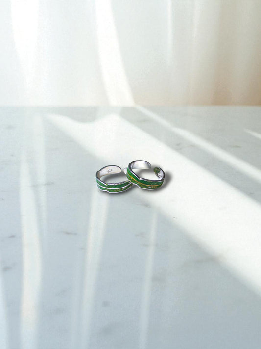 Small toe rings with green accents on a marble surface