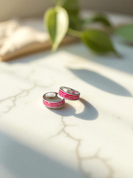 Pair of pink and silver toe rings on a light surface with green leaves in the background