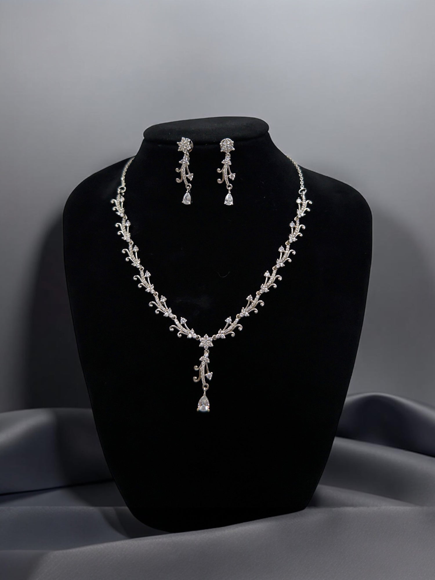 Jewelry set with necklace and earrings on a black bust against a gray background