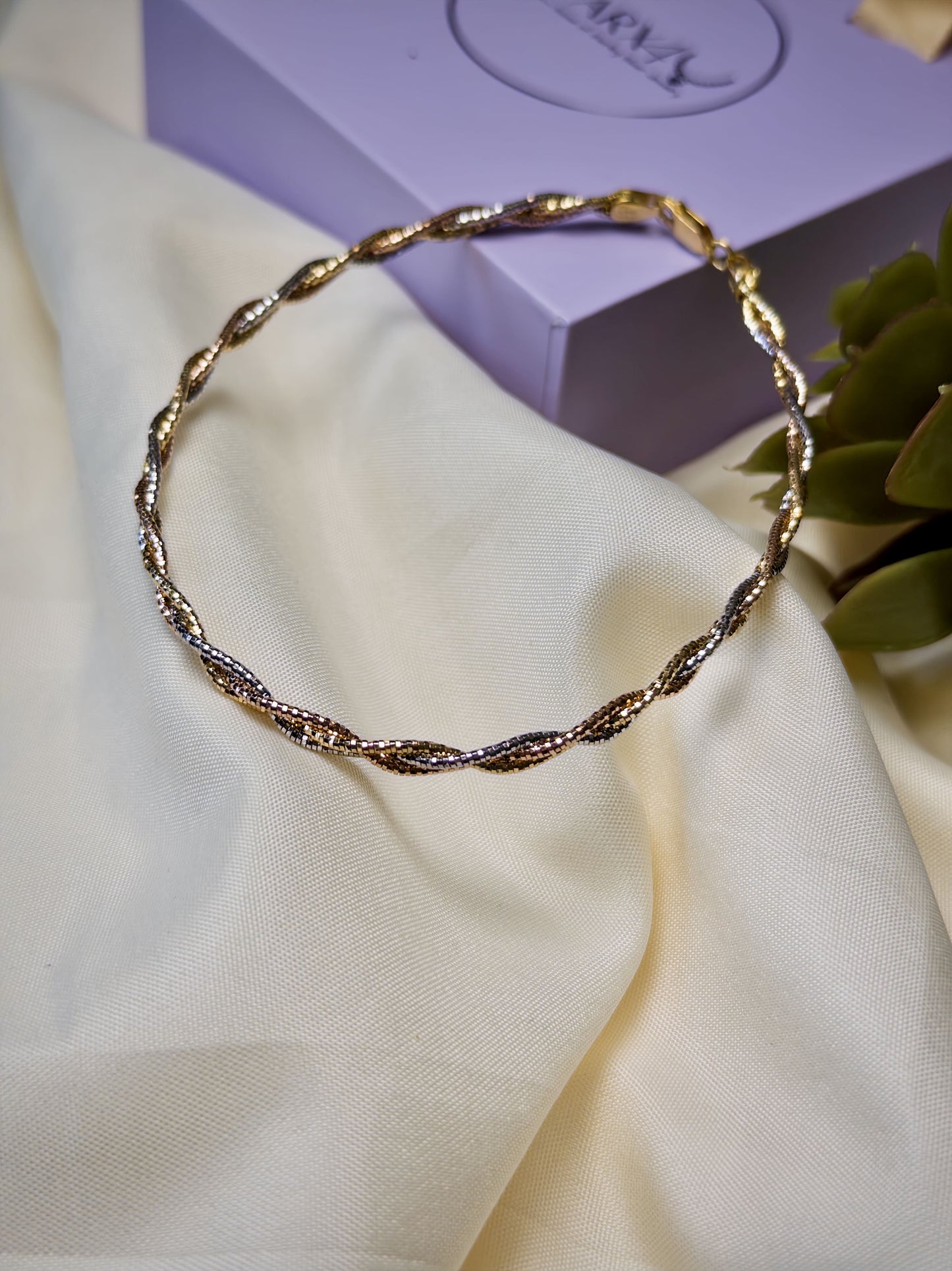 Twisted Gold anklet on a white fabric with a purple box in the background