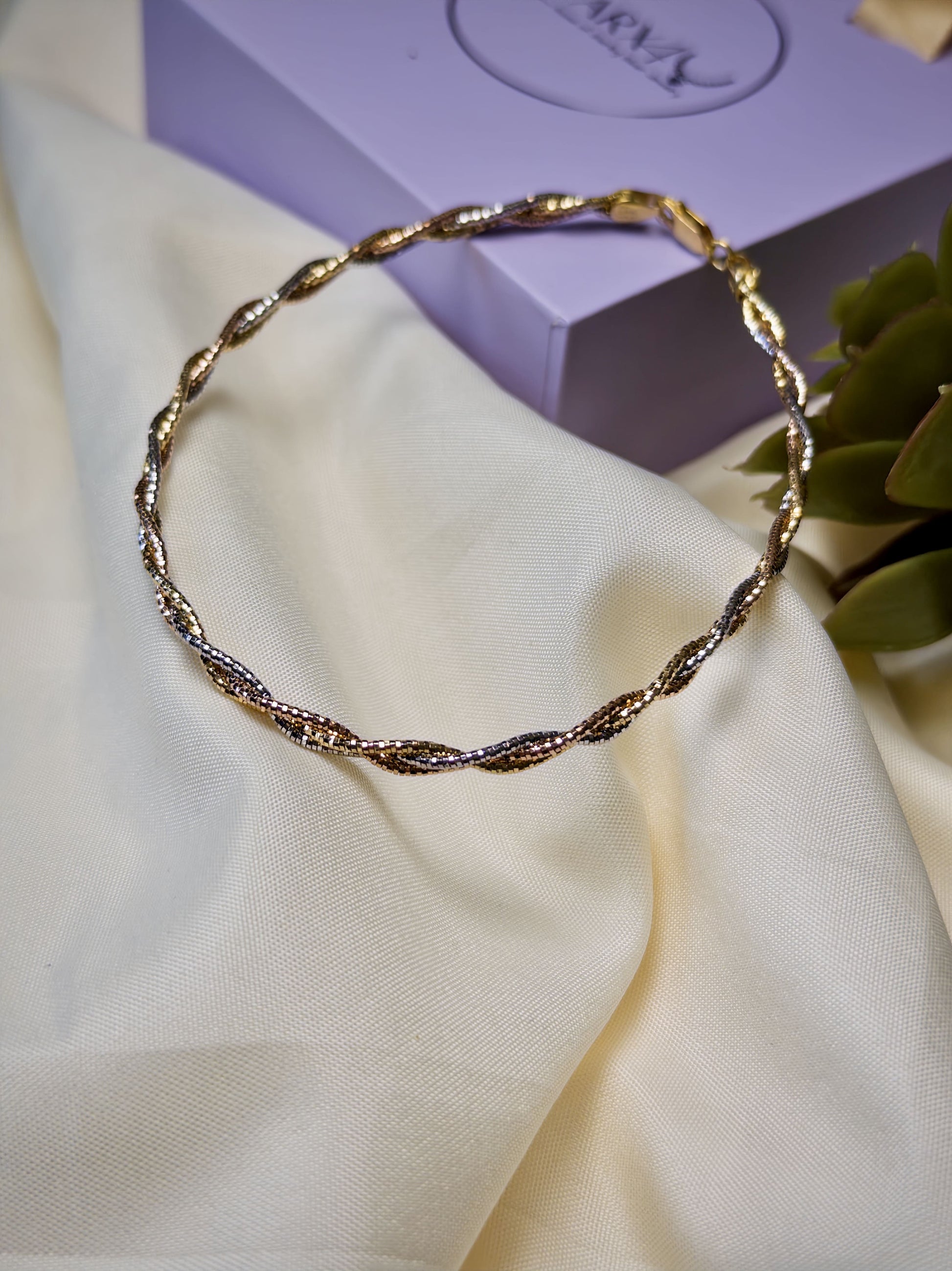 Twisted Gold anklet on a white fabric with a purple box in the background