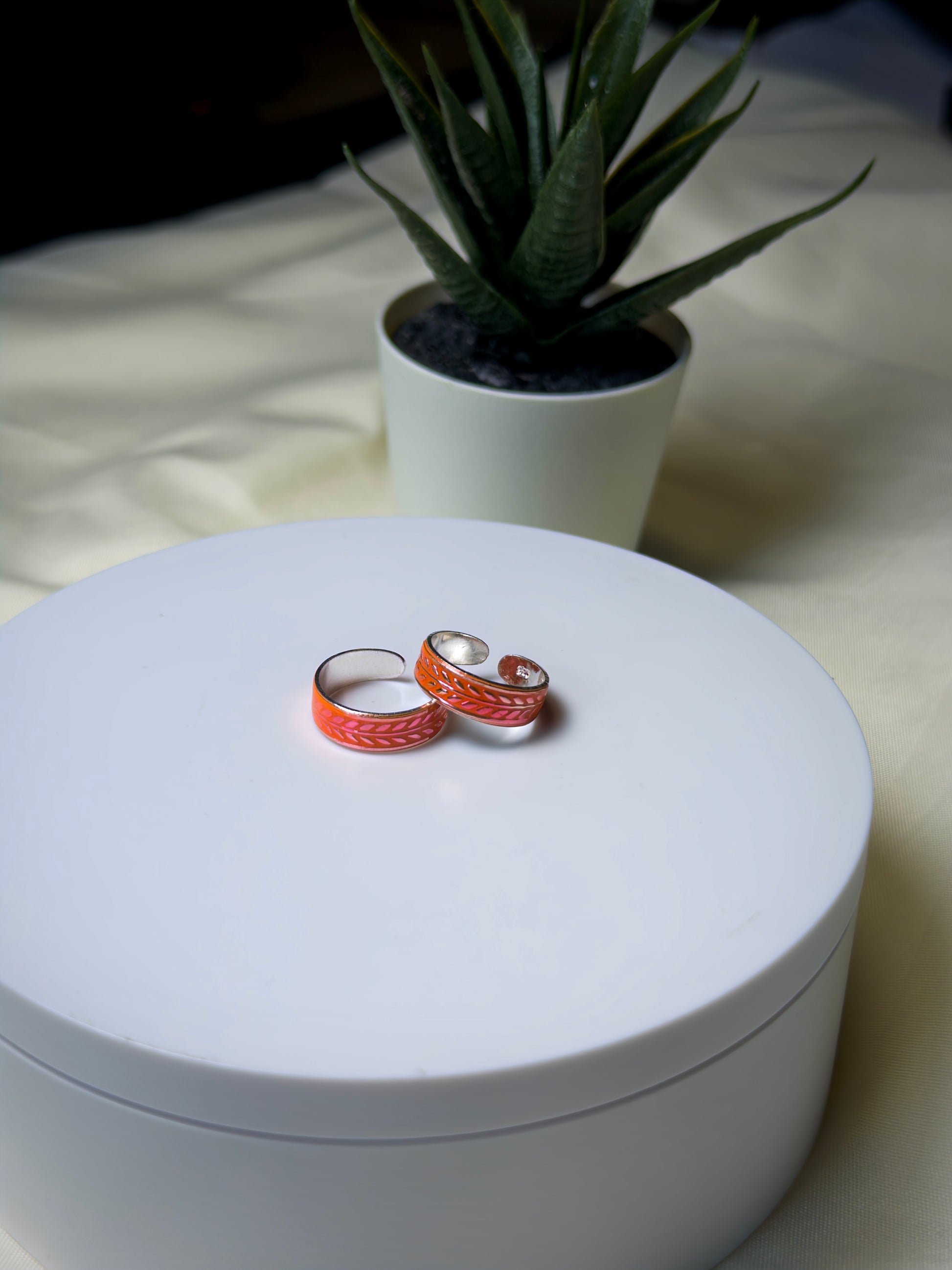Two orange toe rings on a white surface with a plant in the background