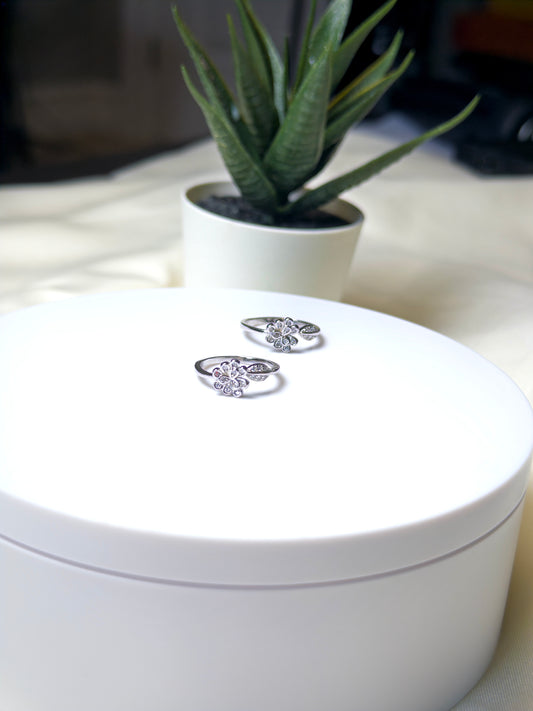 Silver butterfly toe rings on a white jewelry box with a plant in the background