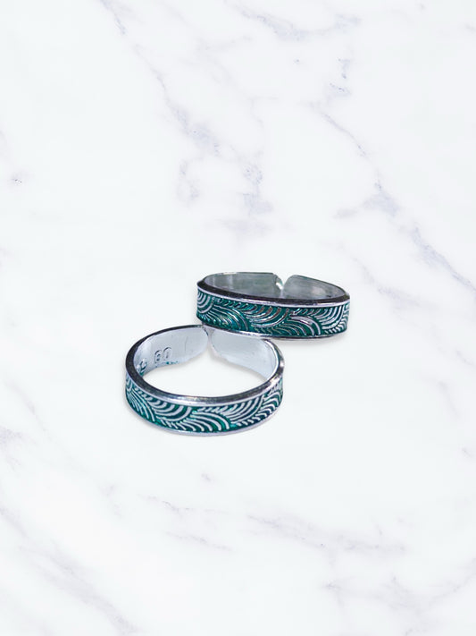 Two silver toe rings with green patterns on a white marble background