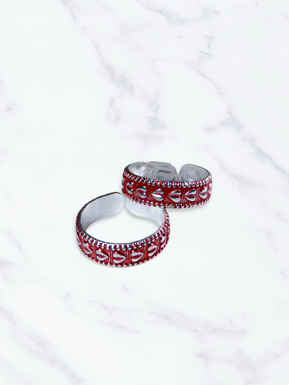 Two red and silver toe rings on a white marble surface