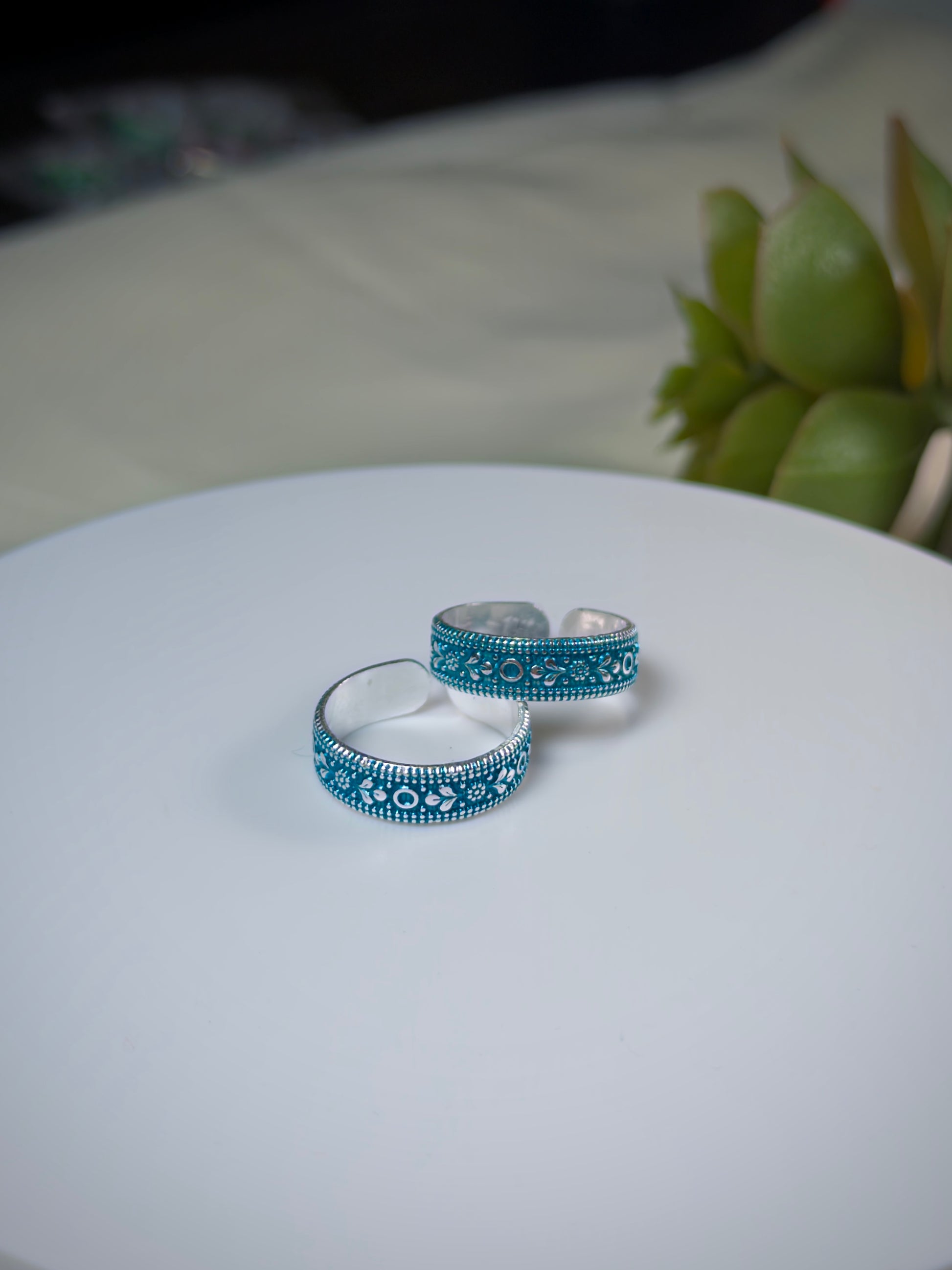 Two silver toe rings with blue patterns on a white surface.
