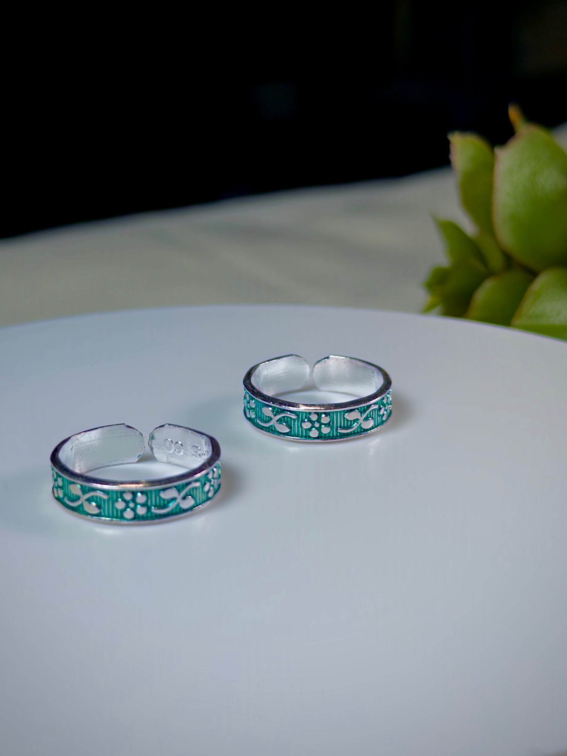 Two silver toe rings with green floral patterns on a white surface.