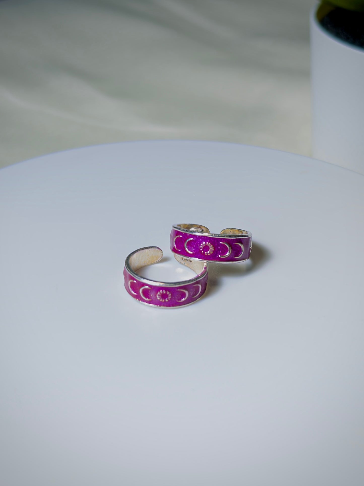 Pair of silver toe rings with pink enamel designs on a white surface