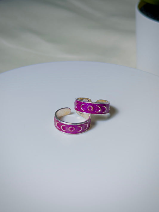Pair of silver toe rings with pink enamel designs on a white surface