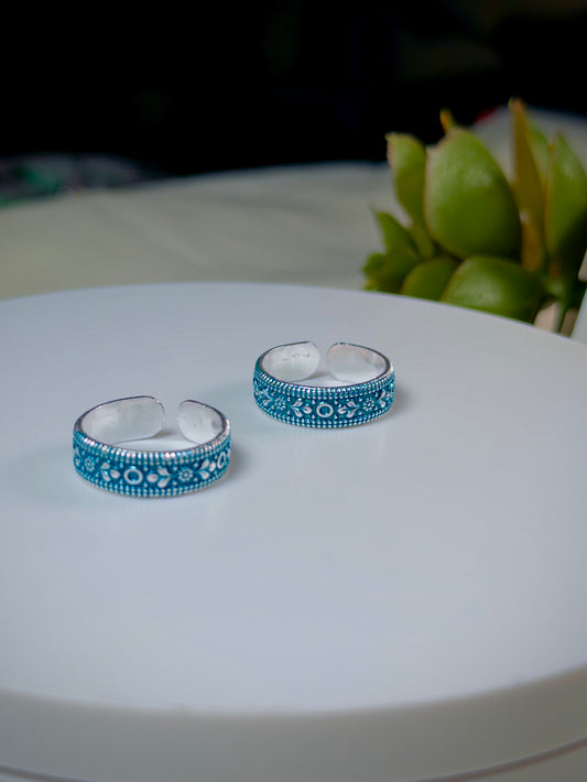 Pair of silver toe rings with blue enameled patterns on a white surface.