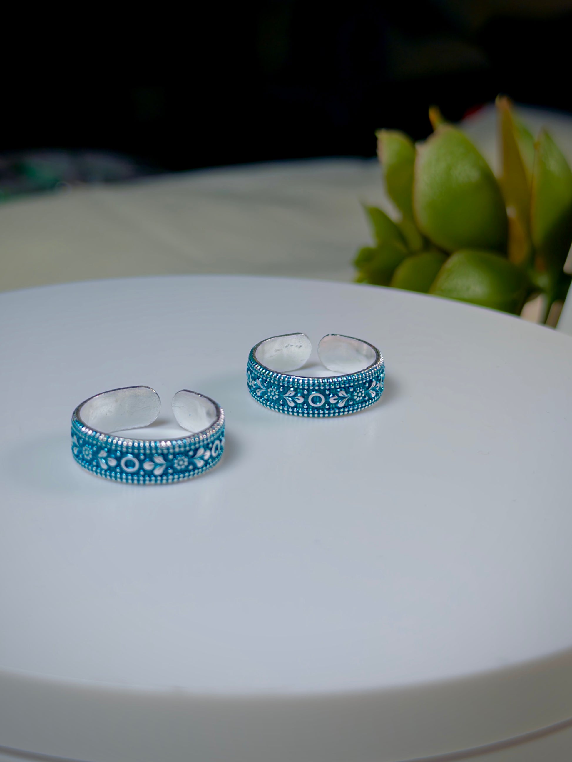 Pair of silver toe rings with blue enameled patterns on a white surface.