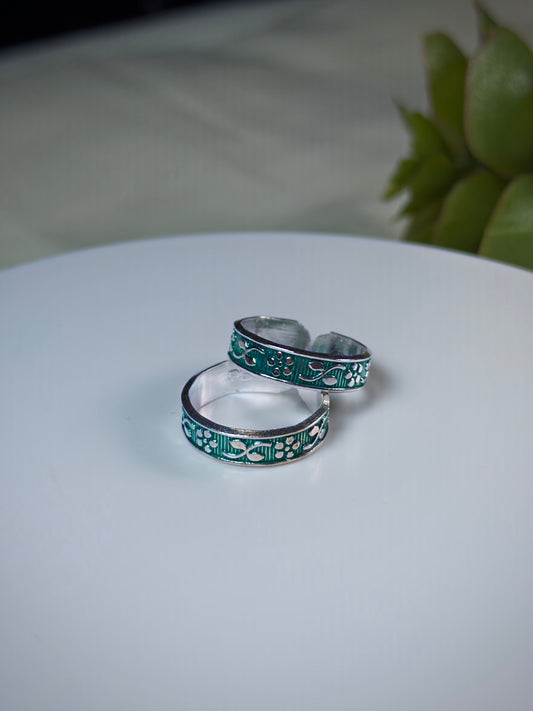 Two silver toe rings with green pattern on a white surface.