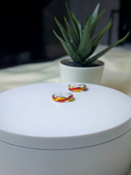 Two toe rings with colorful design on a white surface, with a blurred plant in the background.